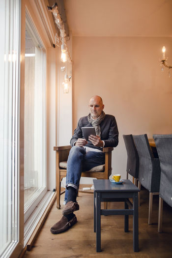 Senior man sitting at home, reading on digital tablet