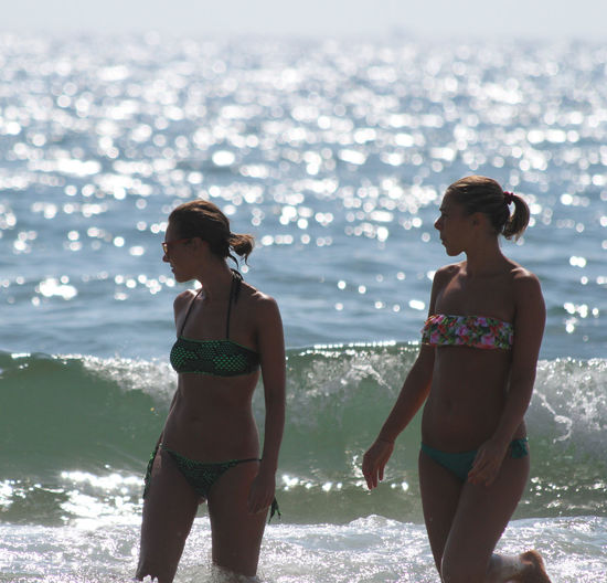 Friends wearing bikini walking in sea during sunny day