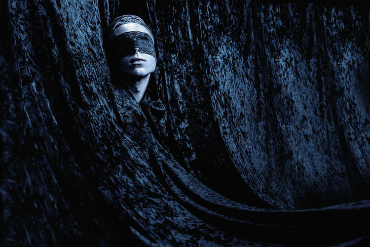 Blindfold man amidst tree trunk at night