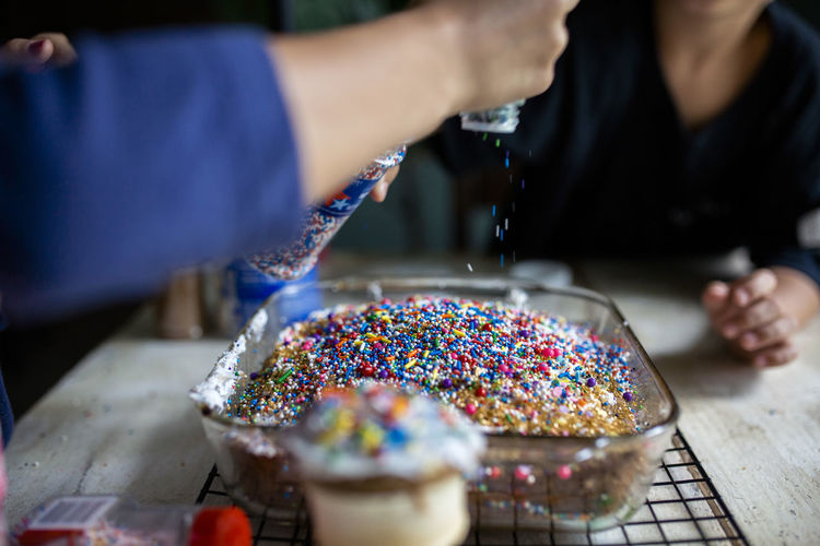 Siblings decorating cake with plenty of colorful sprinkles