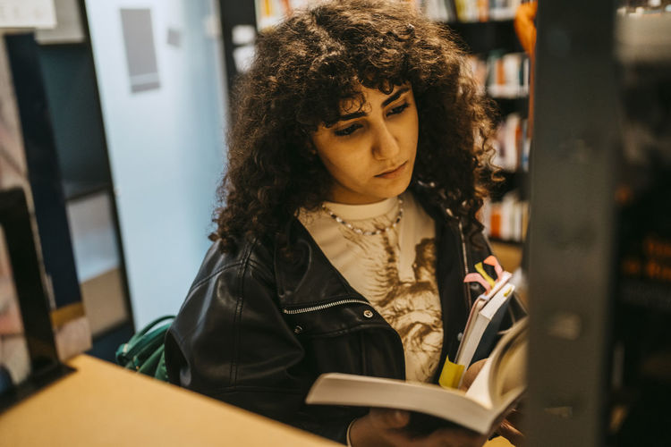 Young female student reading book in college library