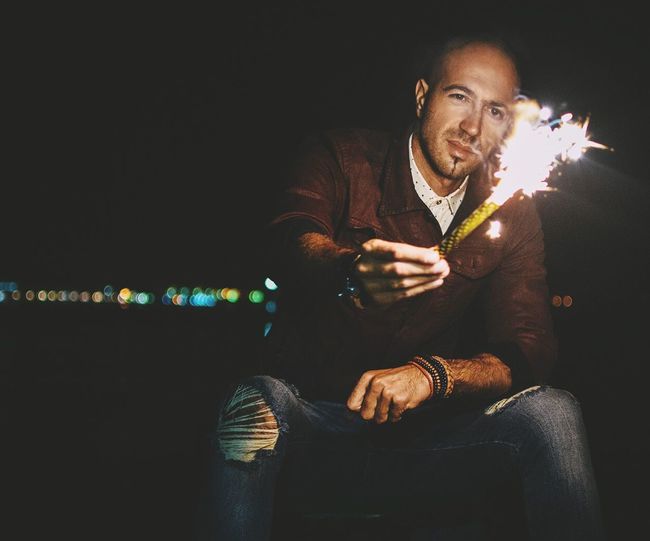 Man holding illuminated cracker at night