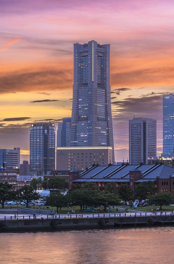 Modern buildings by river against sky during sunset