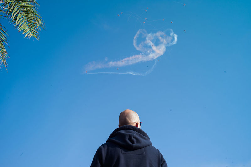 Low angle view of man against vapor trail in sky on sunny day