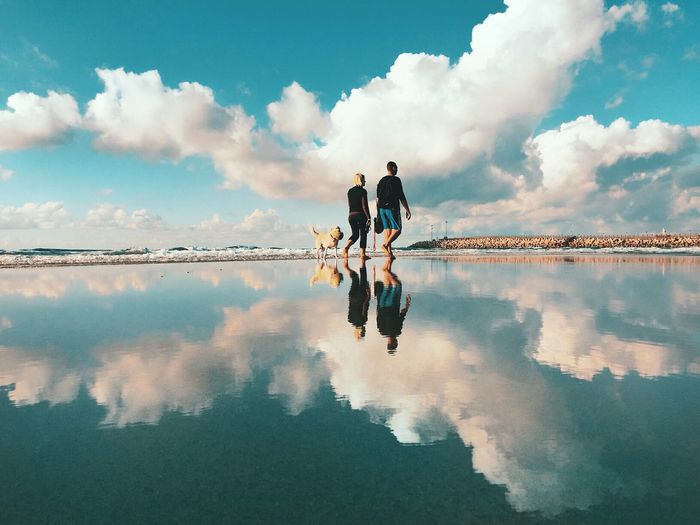 Reflection of people on water against sky