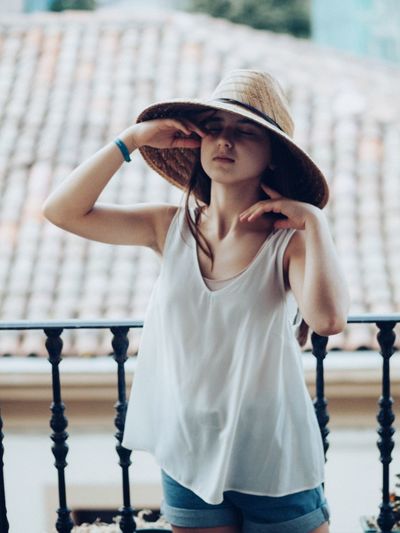 Young woman on the balcony wearing summer clothes and a hat