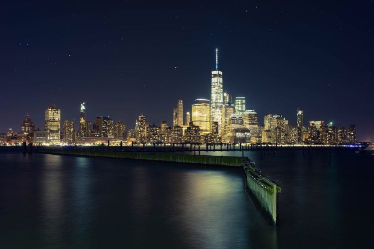 Hudson river by illuminated one world trade center in city at night