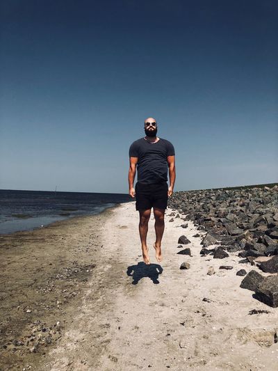 Full length of man levitating on beach against clear sky