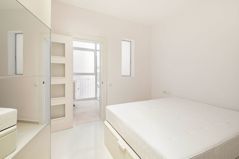 White bedroom with bed, wardrobe and entrance to bathroom in a modern refurbished apartment 
