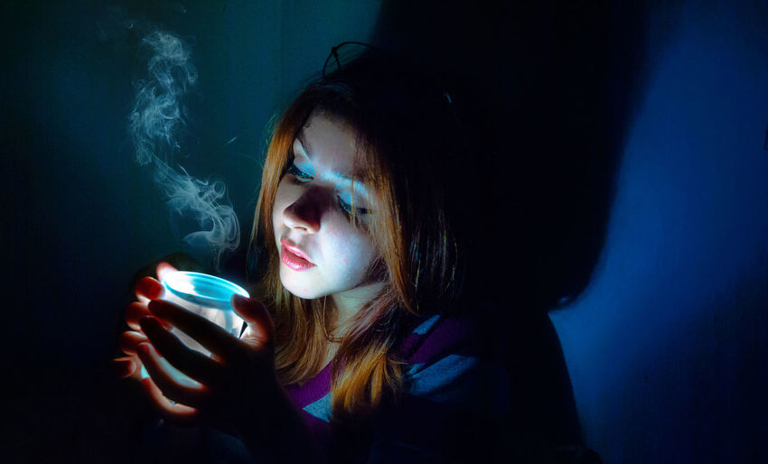 Close-up of woman with illuminated jar with smoke sitting in dark room