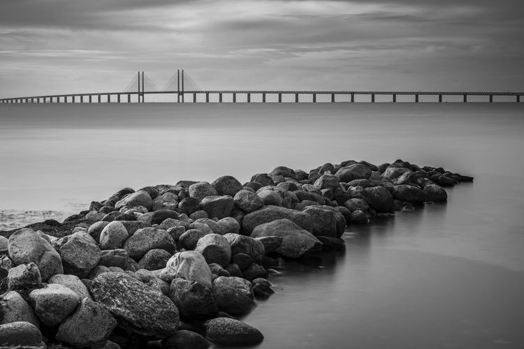 Bridge over rocks in sea against sky