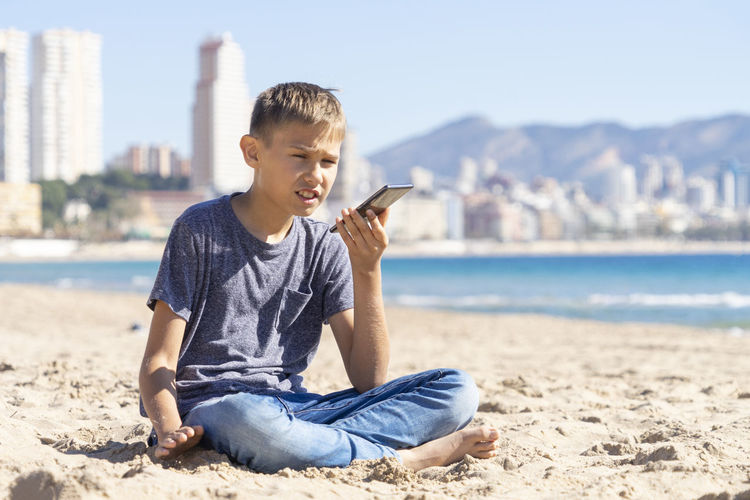 Teenager boy using a smart cell phone voice recognition function, send a voice message on city beach