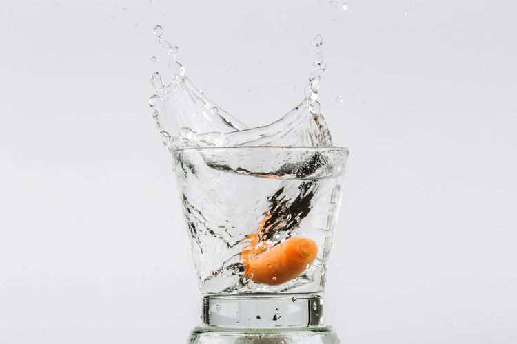Close-up of orange drop on glass against white background