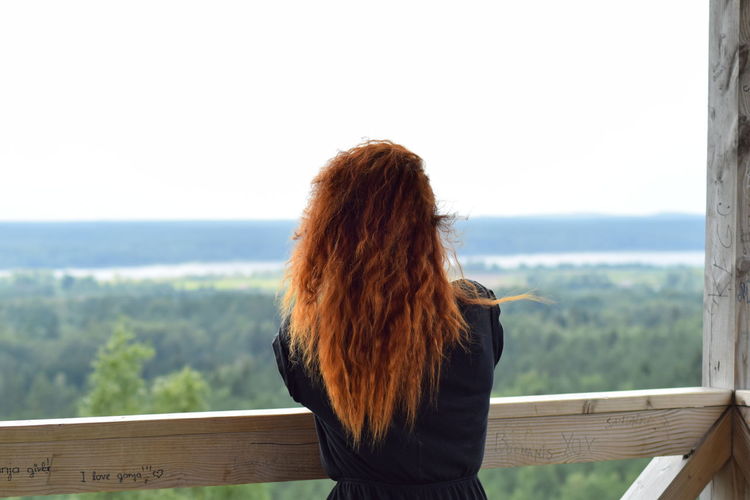 Rear view of woman leaning on railing against green landscape