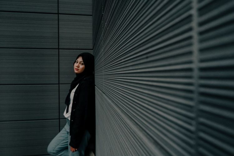 Portrait of a young woman standing against wall