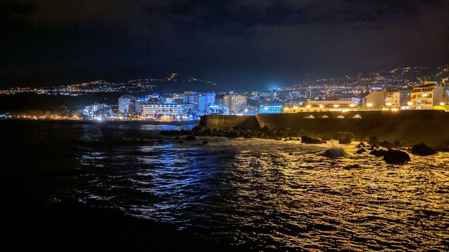 High angle view of illuminated buildings by sea against sky at night