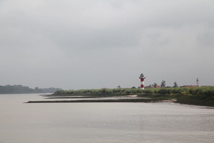 Lighthouse on field by elbe river against cloudy sky