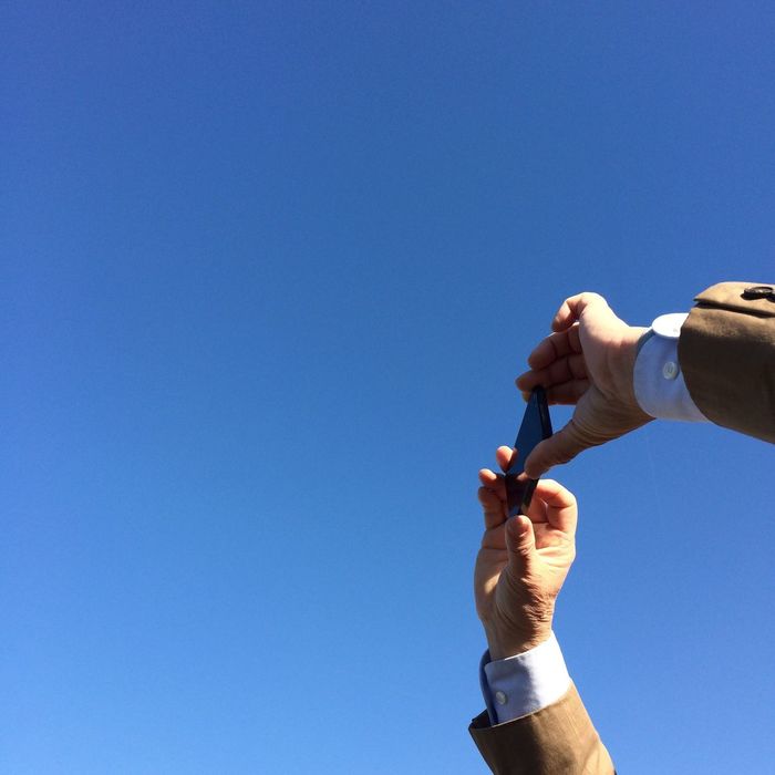 Close-up of hands photographing clear blue sky