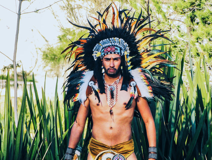 Portrait of shirtless man wearing apache headdress while standing against plants