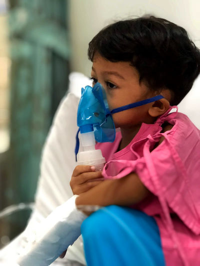 Cute girl with nebulizer on face while sitting in hospital