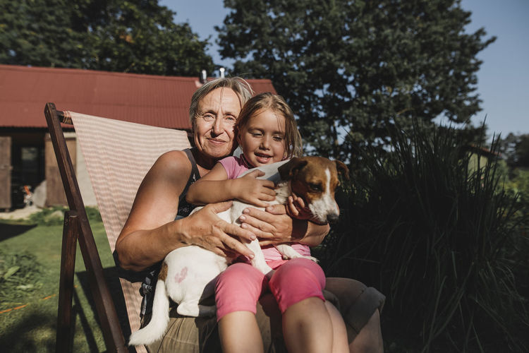 Smiling grandmother with granddaughter and dog on deckchair in garden