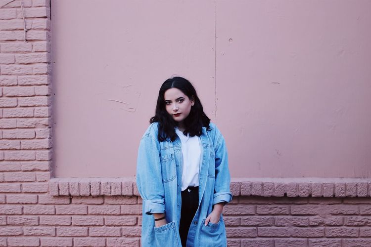 Portrait of young woman standing against wall