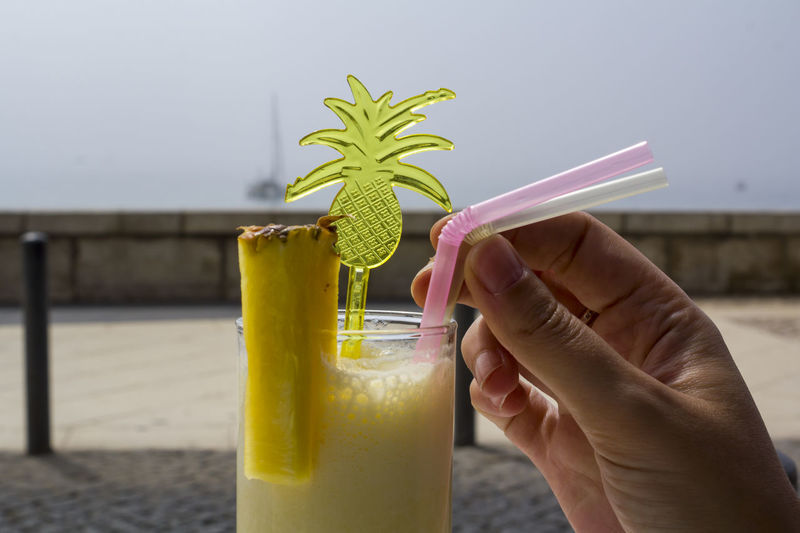 Woman hand drinking a pineapple smoothie cocktail at the beach