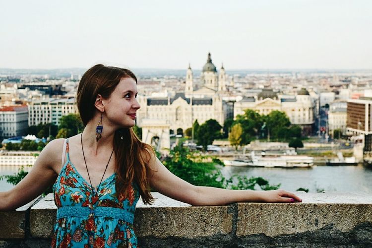 Smiling woman leaning on railing against hungarian parliament building
