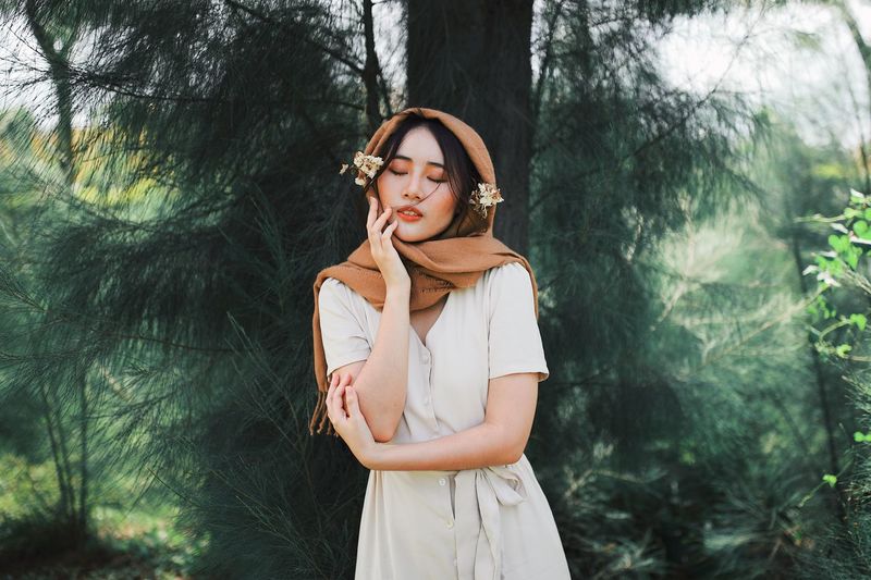Beautiful young woman with eyes closed against trees in forest