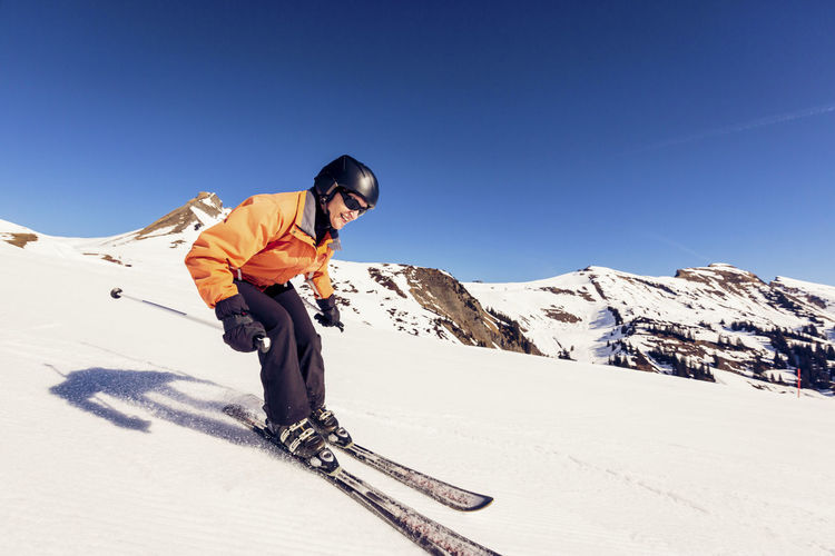 Man skiing on snowcapped mountain against clear blue sky