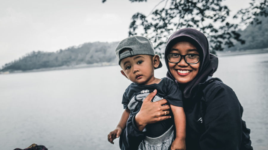 Portrait of smiling mother with son against lake and sky
