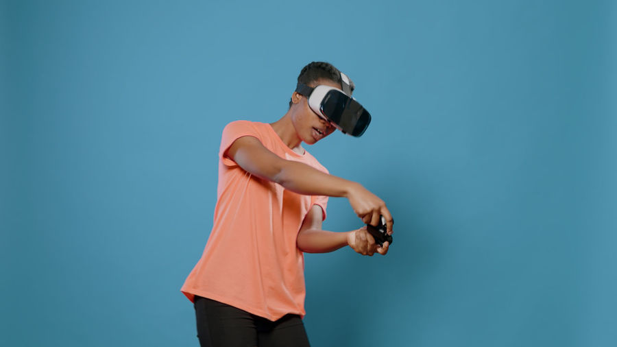 Young woman playing game wearing vr headset against wall
