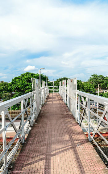 Wooden railway footbridge along plants and bridge against sky