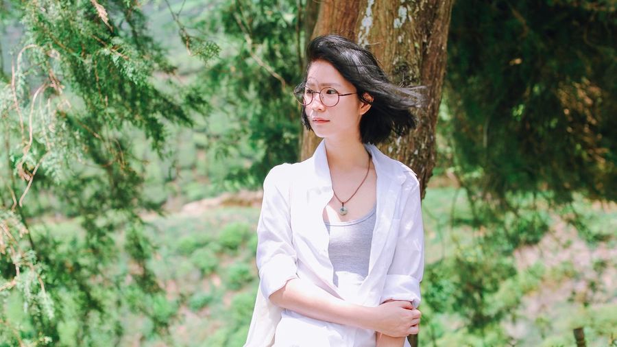 Thoughtful young woman wearing eyeglasses while standing by tree trunk