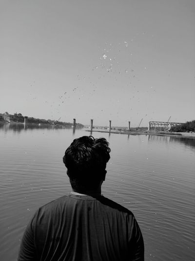 Rear view of man looking at river against sky