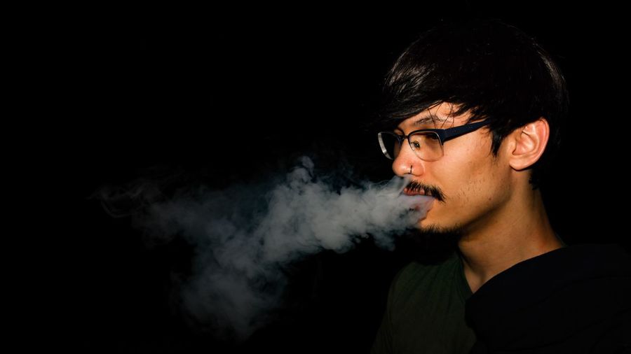 Portrait of young man smoking over black background