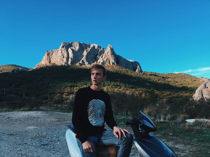 Man sitting on motorcycle against mountains