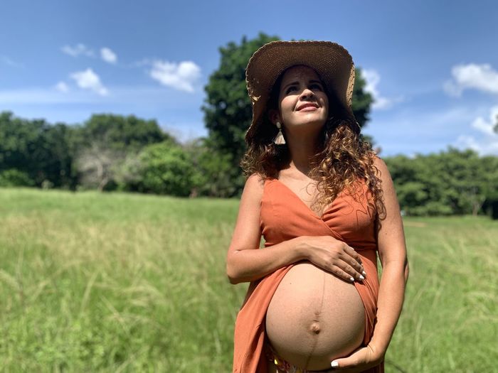 Pregnant woman wearing hat on field against sky