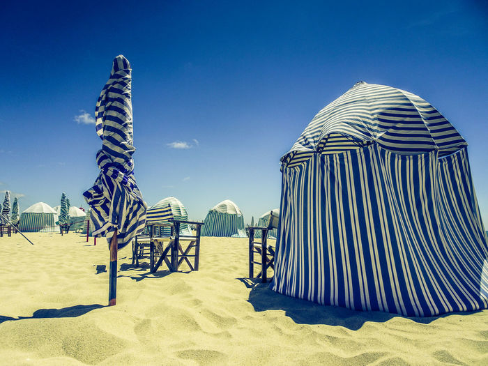 Parasols and tents at beach against blue sky