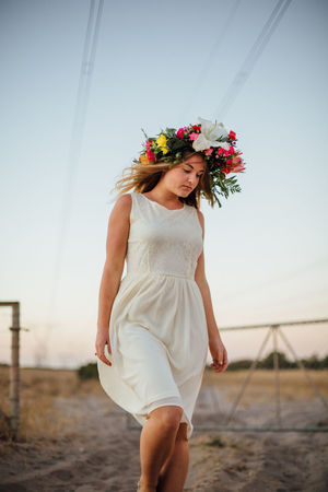 Woman wearing flowers walking on field against sky