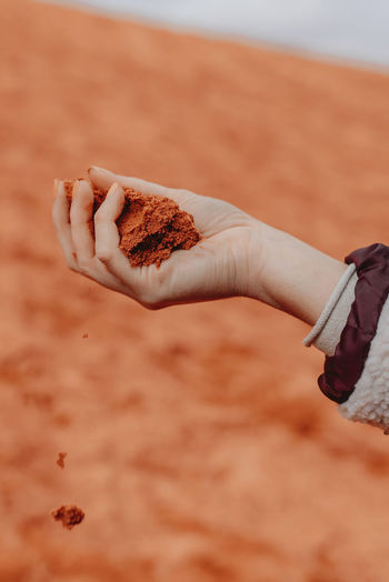 Unrecognizable crop person with handful of red sand standing in wadi rum dry valley in jordan