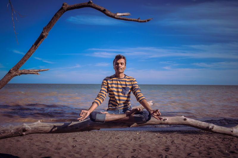 Man doing yoga at beach against blue sky