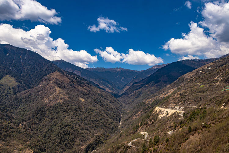 Mountain valley with curvy road and bright blue sky at sunny day from top