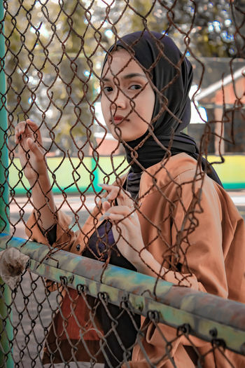 Portrait of young woman standing by chainlink fence