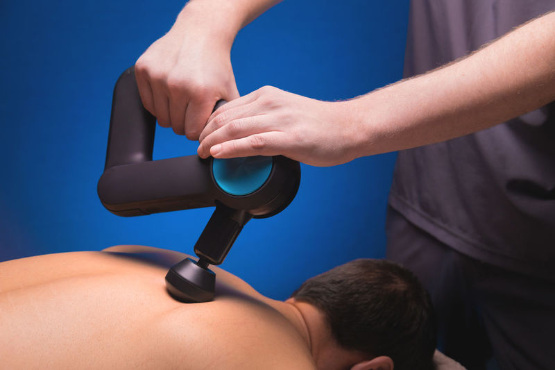 Close-up of a professional male masseur stimulates the back muscles of a male patient in a dark spa