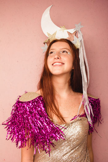 Smiling teenage girl with headdress standing against pink wall