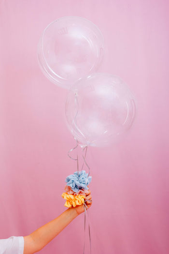 CLOSE-UP OF HAND HOLDING PINK BALLOONS AGAINST WHITE BACKGROUND