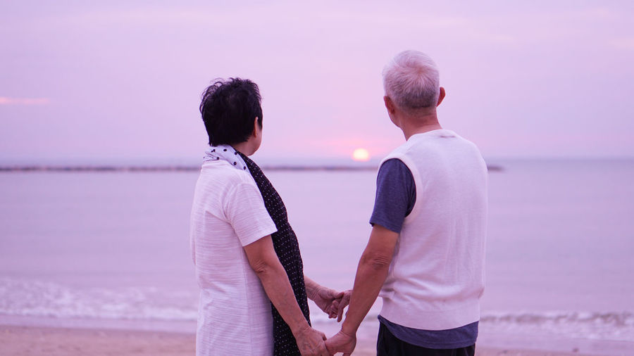Couple standing at beach against sky during sunset