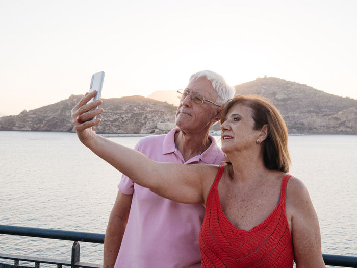 Relaxed senior couple taking a selfie to remember with the seaport beh