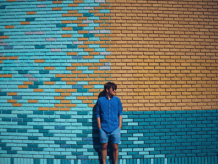 Full length of young man standing against brick wall